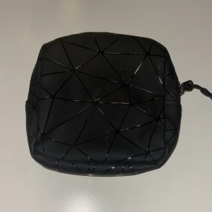 Svart geometrisk mini  necessär  - Snygg svart mini necessär med geometriskt mönster och dragkedja. Perfekt för att hålla små grejer. Finns ett litet fack på insidan 