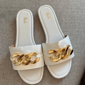 Vita sandaler med gulddetaljer - Stilrena vita sandaler från Shein med bred rem och dekorativa guldkedjor framtill. Perfekta för en somrig look. Helt nya 