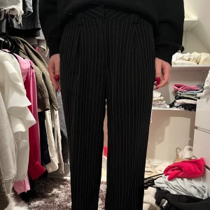 Svarta randiga kostymbyxor - Snygga svarta kostymbyxor med vita ränder. Byxorna har en hög midja och en rak passform som ger en stilren look. Perfekta för en chic och elegant stil.