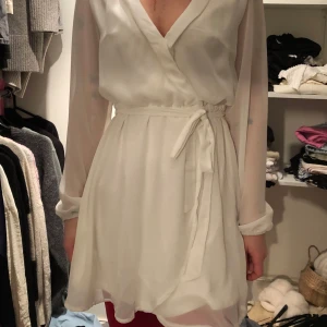 Vit omlottklänning - Elegant vit omlottklänning med långa ärmar och knytband i midjan. Perfekt för en stilren look.