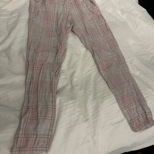 Rutig pyjamasbyxa från KappAhl - Säljer ett par bekväma pyjamasbyxor från KappAhl i rosa och grått rutmönster. Byxorna har en elastisk midja för extra komfort. 