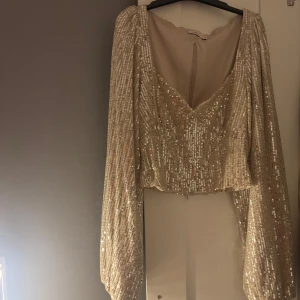 Glittrig champagnefärgad topp - Snygg glittrig klänning i champagnefärg med långa ärmar och v-ringad design. Perfekt för festliga tillfällen, exempelvis nu till nyår!