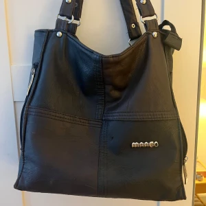 Svart axelväska från Mango - Snygg svart axelväska från Mango i syntetmaterial. Väskan har flera praktiska dragkedjor och ett stilrent utseende. Skinnet har flagnat lite på vissa ställen därav priset. Skriv om ni har frågor💕