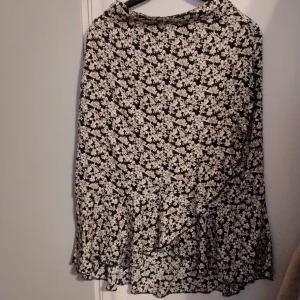 Blommig kjol från lager 157 - Snygg blommig kjol från lager 157 i svart och beiget med volangdetaljer. Perfekt för en trendig look. Kjolen har en omlott-design som ger en fin passform.