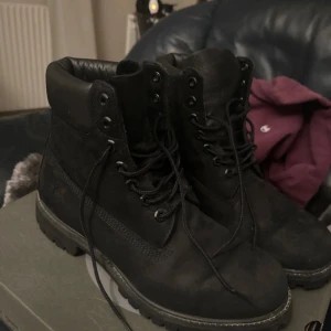 Svarta boots i skinn timberland - Säljer ett par svarta boots från Timberland i äkta skinn. De har snörning och en robust sula, perfekt för kyligare väder. Insidan är fodrad för extra värme och komfort. Lådan som kommer med är till ett annat par äkta timberlands i en annan storlek.