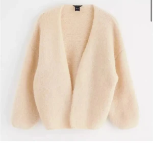 Beige stickad kofta från Lindex  - Mysig beige stickad kofta från Lindex  med en öppen design. Perfekt för lager-på-lager under kyliga dagar. Koftan har en mjuk och fluffig textur som ger en avslappnad look.