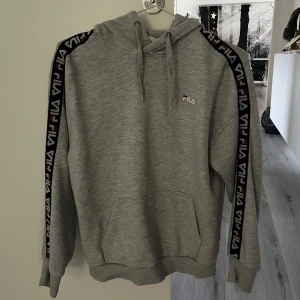 Grå hoodie från Fila - Säljer en grå hoodie från Fila med Fila loggan längs ärmarna. Jag har inte använt den så många gånger, så den är i ett fint skick och inga direkt fläckar som jag har lagt märke till:)