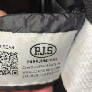 Svart pufferjacka från Parajumpers - Säljer en snygg svart pufferjacka från Parajumpers. Den har en quiltad design med dragkedja och en cool gul detalj vid halsen. Perfekt för höst och vinter, håller dig varm och stilren. Jackan har långa ärmar och en praktisk huva. Passar perfekt för både vardag och festliga tillfällen.