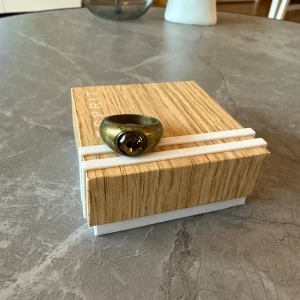 Ny ring med sten - Snygg ny ring med en stor, rund sten i mitten. Ringen har en robust design och en unik färg som ger ett stilfullt intryck. Perfekt för att ge en extra touch till din outfit. Aldrig använd. 18 mm. 