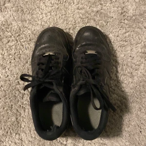 Svarta Nike Air Force sneakers - Svarta Nike Air Force sneakers med klassisk design och snörning. Skorna har en robust sula och perforerade detaljer på ovandelen för ventilation. Perfekta för en stilren look. Box tillgår 