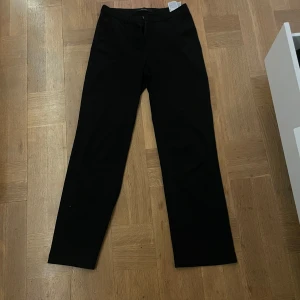 Svarta byxor med dragkedja - Snygga svarta byxor med dragkedja och knapp framtill. De har en rak passform och är perfekta för en stilren look. Materialet ser ut att vara mjukt och bekvämt. (Dålig sista bild, hör av er om ni vlll ha bättre)