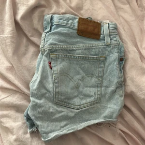 Ljusa jeansshorts från Levi's - Jeansshorts från Levi's, fina till sommaren. Använda en sommar, så ändå välanvända men inga väl synliga skavanker. Högmidjade. W27, resterande mått finns på en av bilderna.