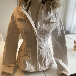 Abercrombie & fitch vit jacka - Säljer en abercrombie & fitch vit jacka med päls luva och päls innuti i storlek M. Dragkedjan är svår att stänga och öppna men går, använder knapparna dock som funkar lika bra. 4 fickor vilket en av de inte går att stänga. 1innerficka. Justebar luva som man kan ta på och av och ett waistband där du även kan justera hur tajt jackan ska sitta. Skriv kring frågor, förhandlingar eller fler bilder på defekterna🩷 