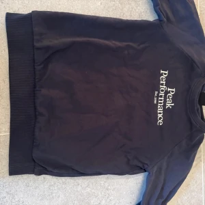 Blå tröja från Peak Performance - Säljer en snygg blå tröja från Peak Performance med vit text på bröstet. Tröjan har långa ärmar och en rund halsringning. Perfekt för en avslappnad stil och varje dag användning. Tveka ej på att fråga!