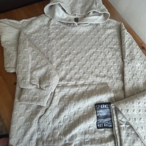 Beige hoodie från SHEIN - Säljer en beige hoodie från SHEIN med ett unikt mönster. Den har en stor ficka framtill och en bekväm huva. Perfekt för en avslappnad stil. Storlek: Medium -38
