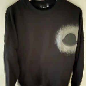 Svart tröja från Palm Angelsx moncler  - Säljer en svart tröja från Palm Angels med ett unikt tryck på framsidan och text på baksidan. Tröjan har långa ärmar och en rund halsringning. Perfekt för en stilren och modern look.