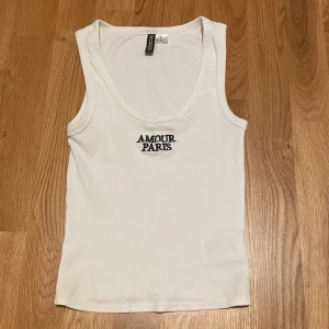 Vit ribbad linnetopp med text - säljer ett vitt ribbat linne ifrån Hm med texten ”amour paris” på bröstet. storlek: XS 