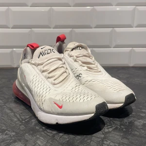 Nike Air Max 270 i vit och röd - Säljer ett par Nike Air Max 270 sneakers i vit med röda detaljer. Skorna har en synlig Air-enhet i hälen och snörning framtill. Tvättas innan de skickas iväg! Perfekta för en sportig look med en modern touch, Bra pris 🔥