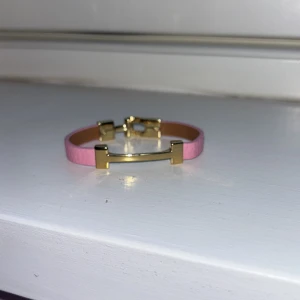 Rosa armband med gulddetaljer - Snyggt rosa armband med eleganta gulddetaljer. Perfekt för att ge en färgklick till din outfit. Armbandet har en stilren design med en smidig låsmekanism.