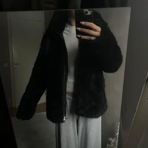 Svart pälsjacka med dragkedja - Säljer en snygg svart pälsjacka med dragkedja. Jackan har en fluffig och varm design, perfekt för kyligare dagar. Den har långa ärmar och en klassisk passform som ger en stilren look.