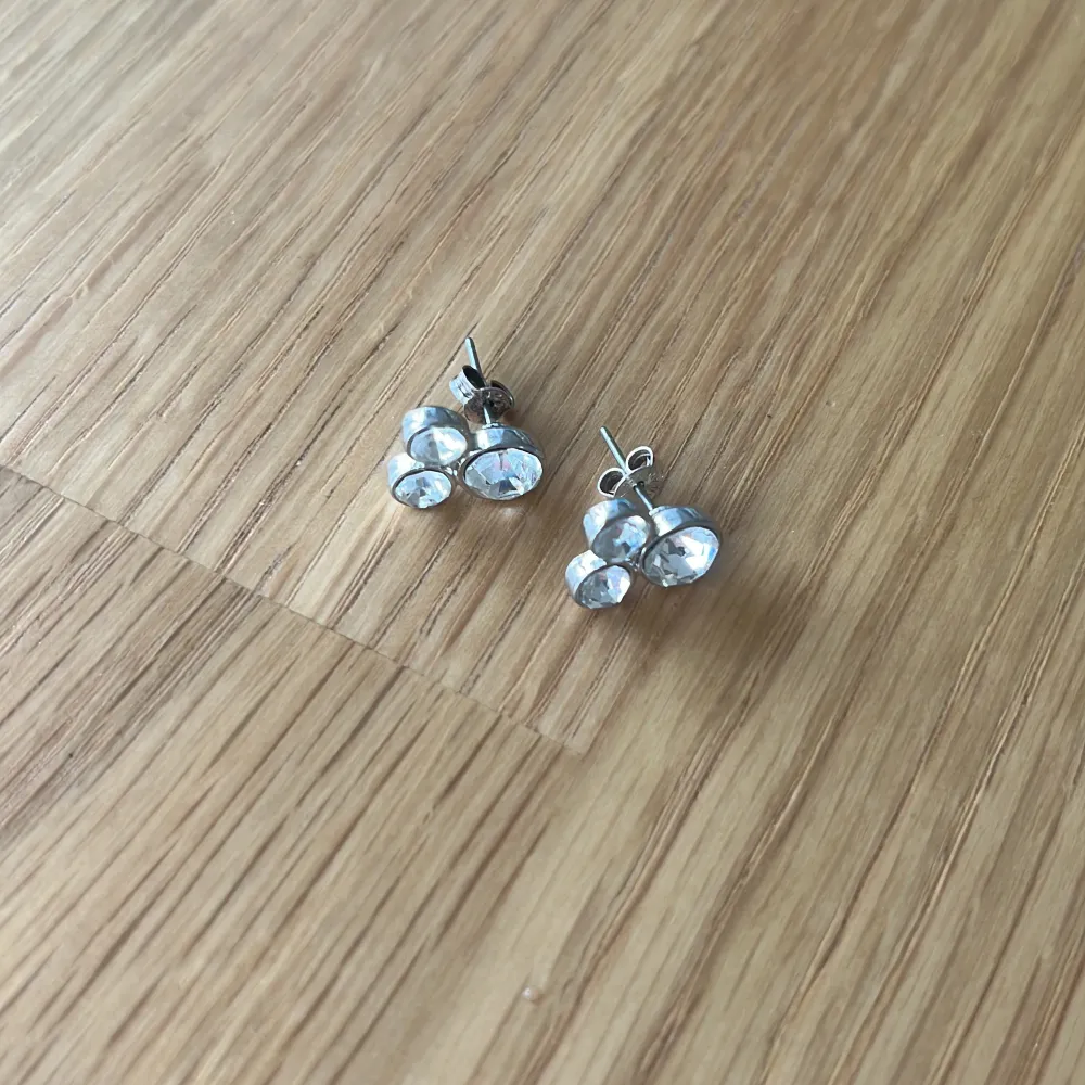Snygga silver örhängen med tre glittrande stenar i varje. Diskreta men ändå iögonfallande då de gnistrar extra mycket i solen. Säljer då jag inte använder silver. Tyvärr finns inte orginalplupparna så därför är de missmatchande, men detta påverkar inte användningen. Örhängena är noga tvättade och disinfekterade. Märket är okänt.. Asusteet.