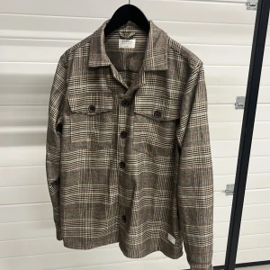 Rutig overshirt från Gabba - Snygg rutig overshirt från Gabba i jordnära färger. Den har långa ärmar och knappar framtill samt två bröstfickor med knappar. Perfekt för lager-på-lager-stil.