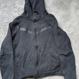 Nike Tech Fleece - Säljer en svart Nike Tech Fleece hoodie från Nike med dragkedja framtill.