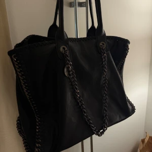 Svart axelväska med kedjedetaljer - Snygg svart axelväska med kedjedetaljer längs kanterna. Väskan har två handtag och en kedja. fint skick! Använd enstaka gång 🖤inköpt i en butik på Marieberg köpcentrum! Märket är Dudlin