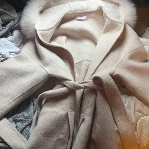 Beige kappa från Born in Stockholm - Säljer en elegant beige kappa från Born in Stockholm. Den har en stor huva med fluffig pälsdetalj och ett knytbälte i midjan. Perfekt för kyliga dagar när du vill hålla stilen. 🧥✨ jätte bra skick och inga skavanker som jag kan se. Endast använd några få gånger. Storlek S men passar mellan xs-m skulle jag säga. 50% ull och 50% cashmere. nypris runt 4500kr. Skriv om du har några frågor💕pris går att diskutera vid snabb handel☺️