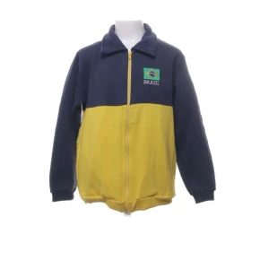 Blå och gul jacka med Brasilien-tema - Säljer en cool blå och gul jacka med Brasilien-tema. Jackan har en dragkedja framtill och broderad text på ryggen. Den är tillverkad av en bomulls- och polyesterblandning, vilket gör den både bekväm och hållbar. Perfekt för dig som vill sticka ut med en unik stil! 💚💛