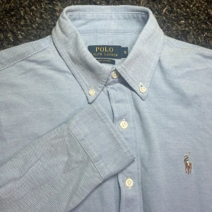 Ralph Lauren skjorta  - Snygg blå skjorta från Ralph Lauren med klassisk krage och knappar. Den har en broderad logga på bröstet och är i knit Oxford material. Cond 9/10. Passar både fest och i vardag! Hör av dig vid minsta lilla fråga!🤩