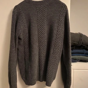 Mörkgrå stickad tröja - Säljer en mysig mörkgrå stickad tröja med ett diskret mönster. Tröjan har långa ärmar och en rund halsringning. Perfekt för kyliga dagar.