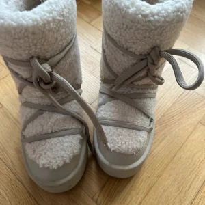 Vita moon boots med snörning från hm - Säljer ett par vita moon boots med snörning. De är tillverkade i ett mjukt och fluffigt material som ger en mysig känsla. Perfekta för kalla dagar. Köpt på Hm