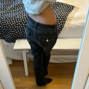 Svarta bootcut jeans med vita sömmar - Snygga svarta jeans med vita sömmar och dekorativa knappar på jackfickorna. Jeansen är bootcut och använda ca 3 gånger. De är ifrån Gina Tricot (Young) och är i storlek 170 (S/M) Det finns även en knapp i midjan som man kan spänna in ifall de midjan skulle vara för stor