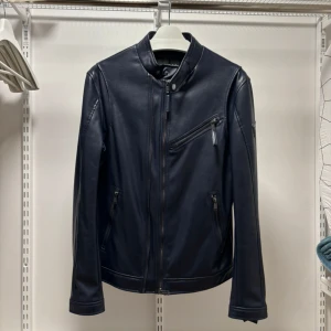 Svart skinnjacka från Guess - Snygg svart skinnjacka från Guess med dragkedja och en cool bröstficka. Jackan har en stilren design med långa ärmar och en liten ståkrage. Perfekt för att ge din outfit en edgy touch.