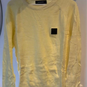 Gul tröja från Peak Performance - Säljer en stilren gul tröja från Peak Performance med lång ärm och en svart fyrkantig logga på bröstet. Perfekt för en avslappnad stil. Tröjan är i storlek M och har en klassisk passform.