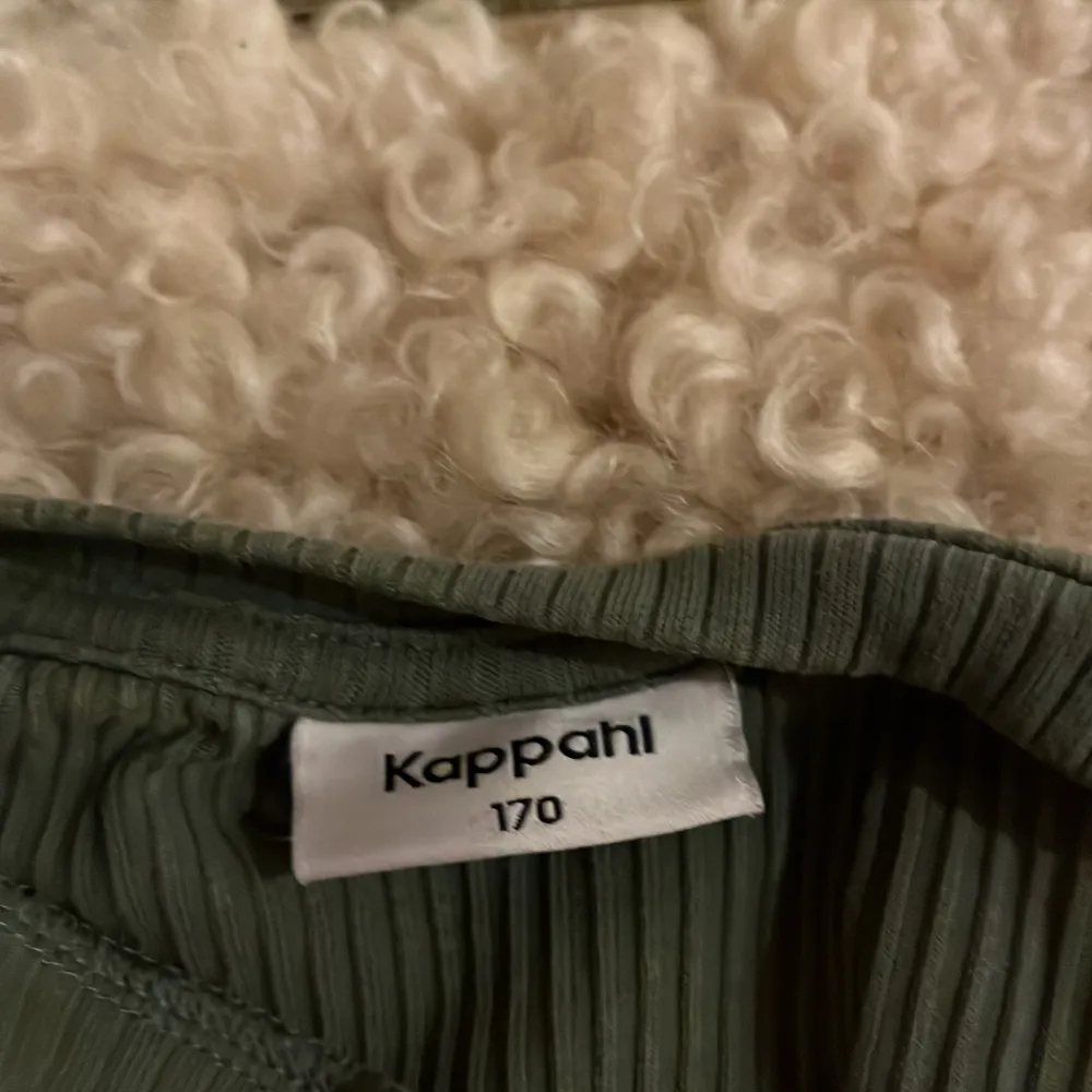 Säljer en snygg grön ribbad topp från Kappahl med volangdetaljer vid ärmarna. Perfekt för en stilren look. Toppen är ärmlös och har en bekväm passform.. Yläosat.