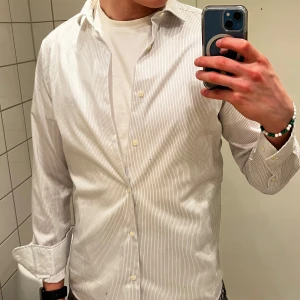 Vit och grå randig skjorta från Pal Zileri - Snygg vit och grå randig skjorta från Pal Zileri i slim fit. Skjortan har långa ärmar och knappar framtill. Perfekt för en stilren look. 