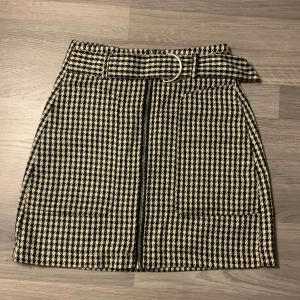 Kjol från Stradivarius, kom gärna med prisförslag!😁 - Snygg rutig kjol från Stradivarius med dragkedja framtill och ett bälte i midjan. Perfekt för att ge en stilren look. Kjolen har en klassisk svart och vit färgkombination.