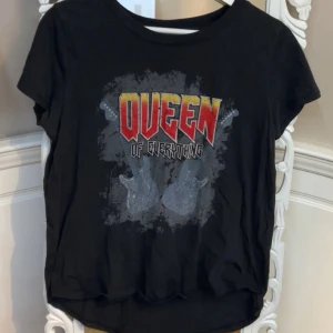 Svart t-shirt med tryck från Gina Tricot - Cool svart t-shirt från Gina Tricot med texten 'Queen of Everything' i rött och gult. Trycket har även två elgitarrer i grått. Perfekt för en rockig look! 🎸