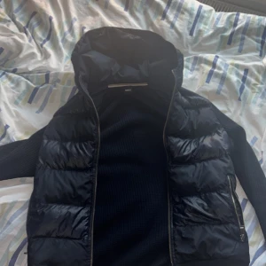 Marinblå cardigan från Hugo boss - Säljer en snygg marinblå jacka från Boss med quiltad design och dragkedja. Jackan har långa ärmar och en huva, perfekt för kyligare dagar. Den är både stilren och funktionell. Den är storlek S men passar M (stor i storlekar) Kan mötas upp i Upplands Väsby eller fraktas