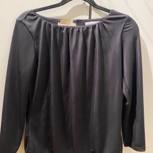 Svart trekvart ärmad topp från H&M - Snygg svart trekvart ärmad topp från H&M med en elegant drapering framtill. Perfekt för en stilren look. Tillverkad i ett mjukt och bekvämt material.