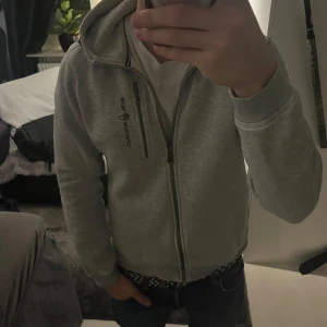 Grå Sail Racing Hoodie - Säljer min stil racing tröja då den blivit för liten. Den är i ganska bra skick utan hål eller liknande men det är en liten slitning på ena armbågen som man kan se på bilden.