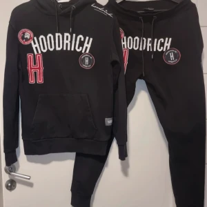 Svart hoodrich dress st small - Säljer en svart dress från Hoodrich med vita och röda detaljer. Tröjan har en stor ficka framtill och justerbar huva med dragsko. Märkets logga och text finns tryckt på framsidan tillsammans med flera patches. en supersnygg o skön dress Hund finns I hemmet 