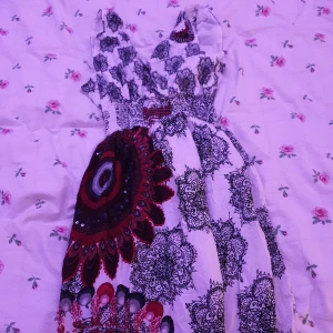 Mönstrad klänning med v-ringning - Säljer en unik klänning med v-ringning och ett iögonfallande mönster i svart, rött och vitt. Klänningen har ett elastiskt band i midjan för en bekväm passform. Perfekt för dig som vill sticka ut!