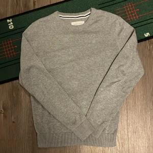 Grå tröja från Pier One - Säljer en stilren grå tröja från Pier One. Tröjan har en rund halsringning och långa ärmar. Perfekt för en avslappnad look. Passar bra till både jeans och chinos. Storlek XS passar folk runt 168-174 helt ny använd en gång.