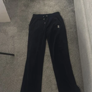 Mörkblå byxor från Juicy Couture - Snygga mörkblå byxor från Juicy Couture med glittrande text på baksidan. Byxorna har en bekväm passform och dragsko i midjan för justerbarhet. Perfekta för en avslappnad stil med en touch av glamour.
