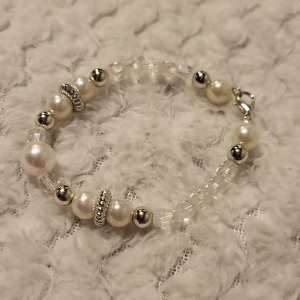 Elegant armband med pärlor och silverdetaljer - Snyggt armband med vita pärlor och silverfärgade detaljer. Armbandet har en mix av större och mindre pärlor samt glittrande silverkulor och dekorativa ringar. Perfekt för att ge en elegant touch till din outfit.