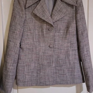 Grå rutig kavaj - Snygg grå rutig kavaj med klassisk krage och knappar framtill. Perfekt för en stilren look. Passar bra till både jeans och mer formella byxor.