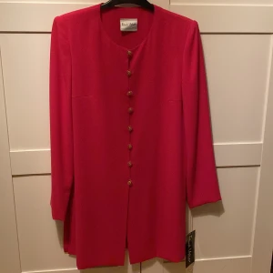Röd kappa från Frank Usher | Nypris 2395 - Snygg röd kappa från Frank Usher med eleganta guldknappar. Den har en stilren design med långa ärmar och en rak passform. Perfekt för att ge en färgklick till din outfit. Helt i nytt skick aldrig använd!